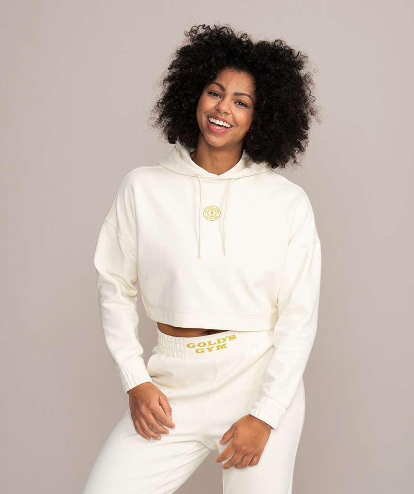 White women's cropped hoodie from Gold's Gym. Women's long sleeve cropped hooded top with drawstrings and Gold's Gym Weight Plate logo on the front. 